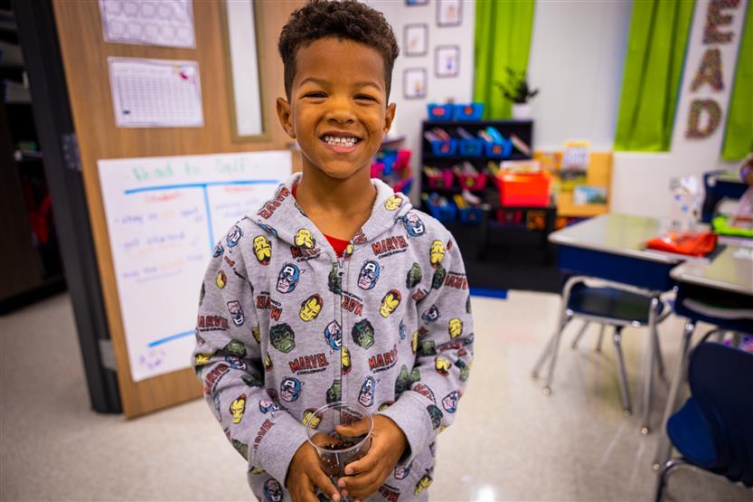 A boy smiles while holding a seed in a cup